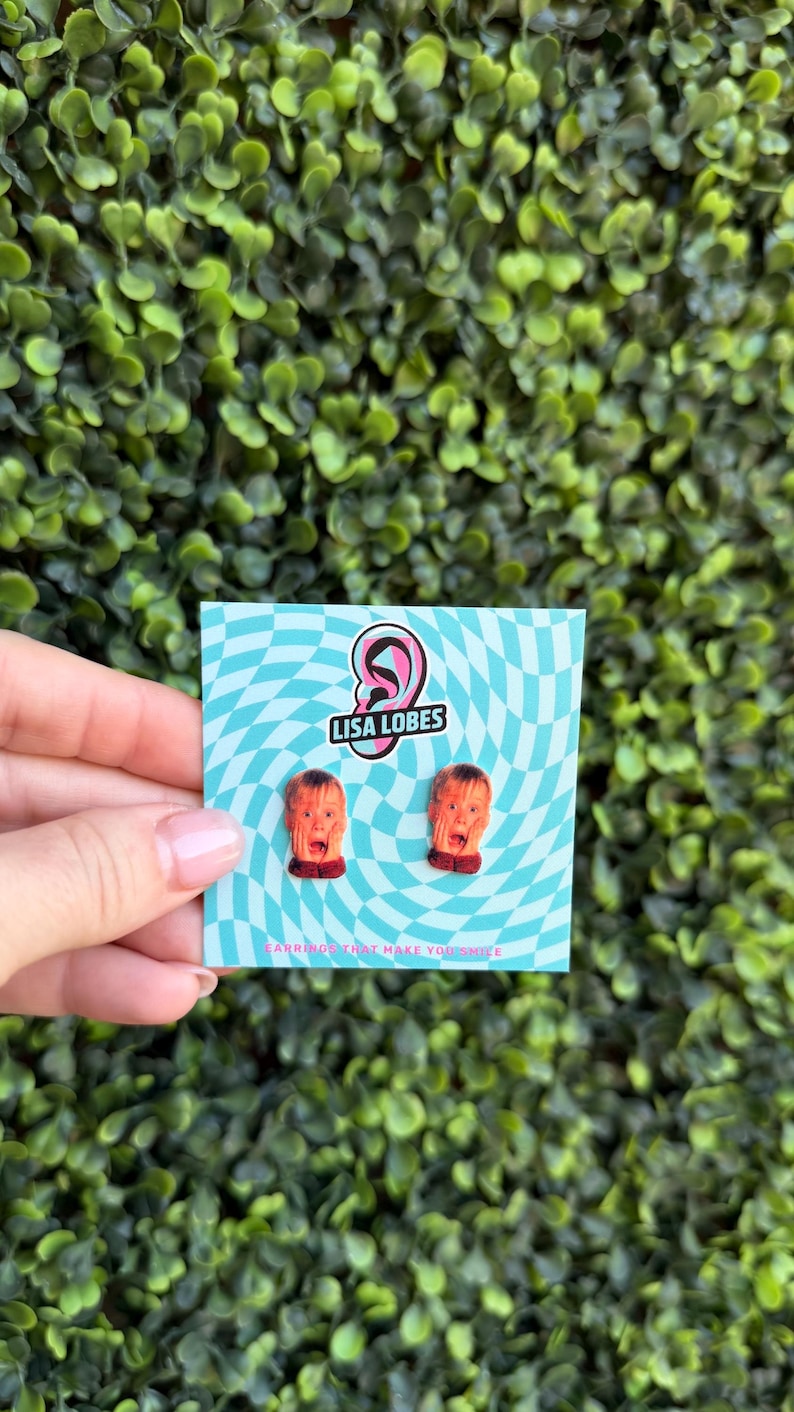 Pu&ograve; includere: Orecchini originali con un design a forma di volto che urla. Sono presentati su una carta a motivi blu e bianchi con il testo "LISA LOBES" e "EARRINGS THAT MAKE YOU SMILE".