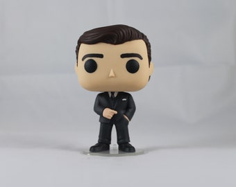 May include: A black and white pop vinyl figure of a man wearing a black suit and a white shirt with a black tie. The figure has brown hair and a serious expression.