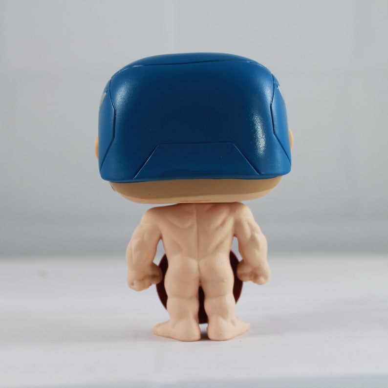 May include: A vinyl collectible figure featuring a stylized character with a large head and a blue helmet. The figure has a muscular, light-toned body and is shown from the back, revealing a dark red circular shield held at the side.