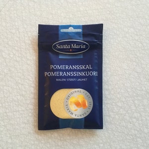May include: A dark blue packet of Santa Maria brand pomeransskal, a spice made from dried orange peel. The packet has white text and a circular logo with orange peel illustrations. The text "ORIGINAL EST. 1911" is also visible.