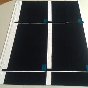 May include: A black and white textile with a geometric design. The fabric features large black rectangles separated by white lines. Small teal squares accent the intersections of the lines, creating a modern, abstract pattern. The edges are finished with a white border.