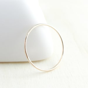 Peut inclure: Un bracelet jonc fin de couleur or. Le bracelet circulaire est présenté sur une surface en bois clair, avec un fond blanc. Le design minimaliste du jonc le rend adapté au port quotidien.