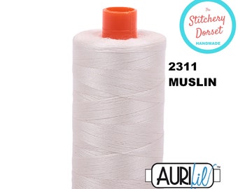 May include: A spool of white muslin thread with an orange top and base. The spool has the text "2311 MUSLIN" and the Aurifil logo. The Stitchery Dorset Handmade logo is also visible.