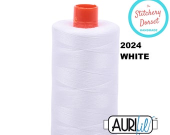 May include: A white spool of Aurifil thread with a red top and bottom. The spool is labeled "2024 WHITE" and has the Aurifil logo on the side. The The Stitchery Dorset logo is in the upper right corner.