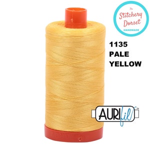 May include: A spool of pale yellow thread with the brand name "Aurifil" and the number "1135" printed on the label. The label also says "Pale Yellow".