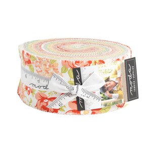 Könnte beinhalten: Ein gerolltes Bündel Stoffstreifen mit einem Blumenmuster in Rot-, Pfirsich- und Weißtönen. Der Stoff ist mit einem weißen Band umwickelt, das mit Zentimetermessungen und dem Wort "mod" bedruckt ist. Ein schwarzes Etikett mit dem Wort "moda" ist angebracht.