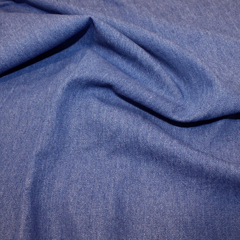 May include: A close-up of a blue denim fabric with a textured weave. The fabric is folded and draped, showing its soft and pliable texture.