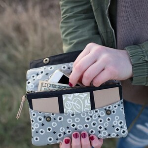 May include: A gray and black fabric wallet with a zipper closure and multiple pockets. The wallet is open and contains a cell phone, cash, and cards.