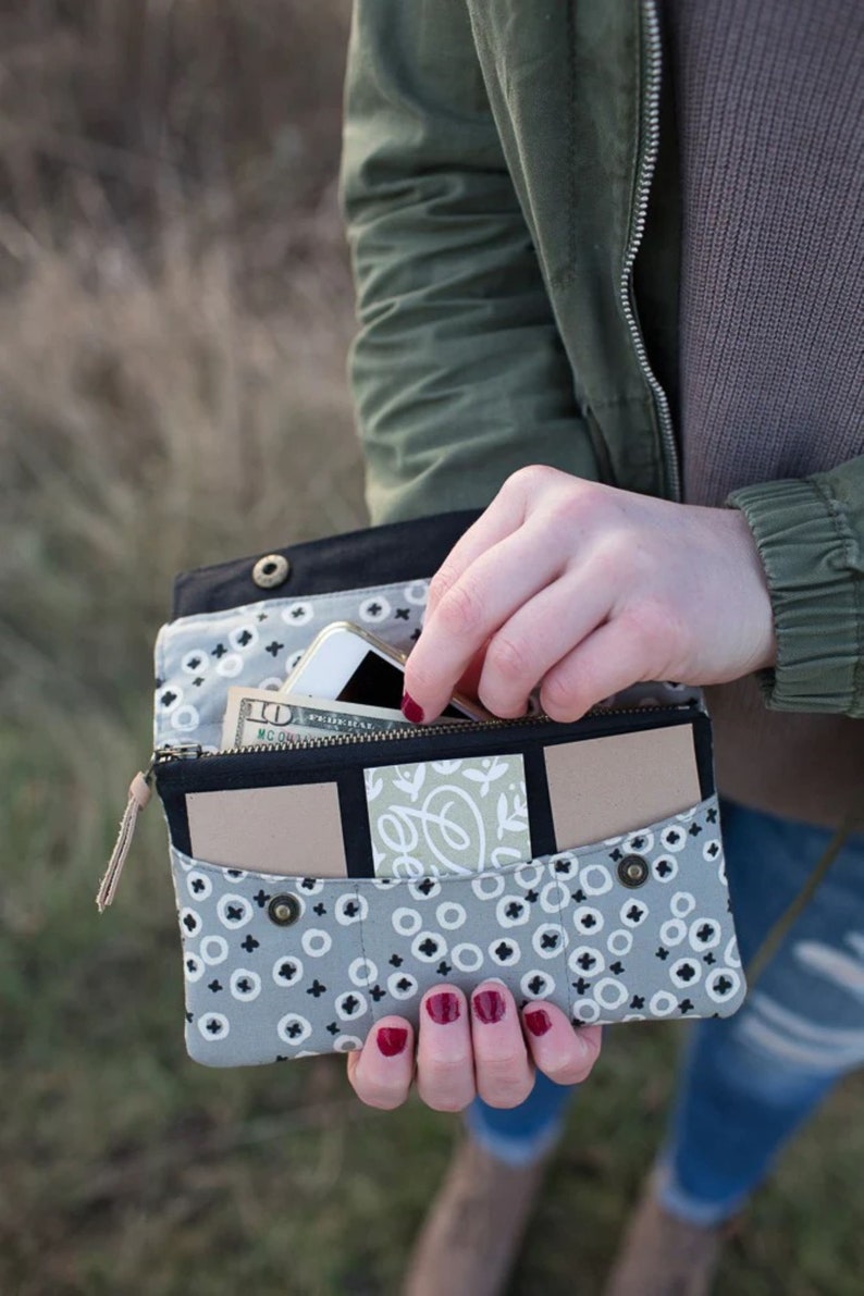 May include: A gray and black fabric wallet with a zipper closure and multiple pockets. The wallet is open and contains a cell phone, cash, and cards.