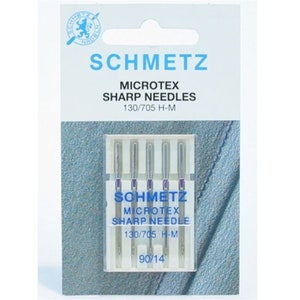 Puede incluir: Un paquete de seis agujas de coser plateadas etiquetadas "Schmetz Microtex Sharp Needles 130/705 H-M 90/14".