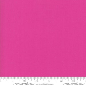 May include: A solid pink fabric swatch with a ruler showing measurements in inches. The ruler has the word "moda" printed on it.