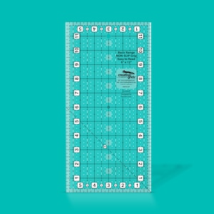May include: A clear plastic ruler with a grid pattern and inch markings. The ruler is 6 inches by 12 inches and has a non-slip grip. It is labeled "Basic Range NON-SLIP Grip Easy to Read 6" x 12" Creative Grids".