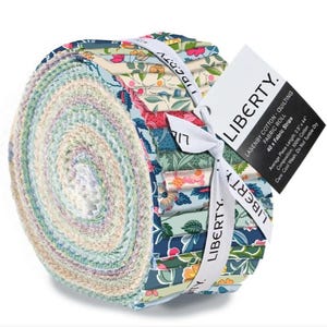 Peut inclure: Un rouleau de bandes de tissu à motifs, noué avec un ruban blanc. Le tissu présente des motifs floraux dans des tons de bleu, rose et vert. Une étiquette indique "LIBERTY" et "LASENBY COTTON - QUILTING". Chaque bande mesure 6,35 cm x 111,76 cm.