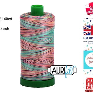 Könnte beinhalten: Eine Spule Aurifil 40wt Garn in Farbe 3817, genannt "Marakesh". Das Garn ist eine mehrfarbige Mischung aus Rosa, Türkis, Gelb und Lila.