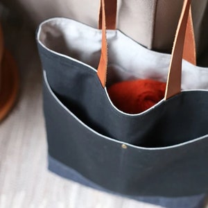May include: A black canvas tote bag with leather handles. The bag has a white lining and a small pocket on the front. The bag is empty.