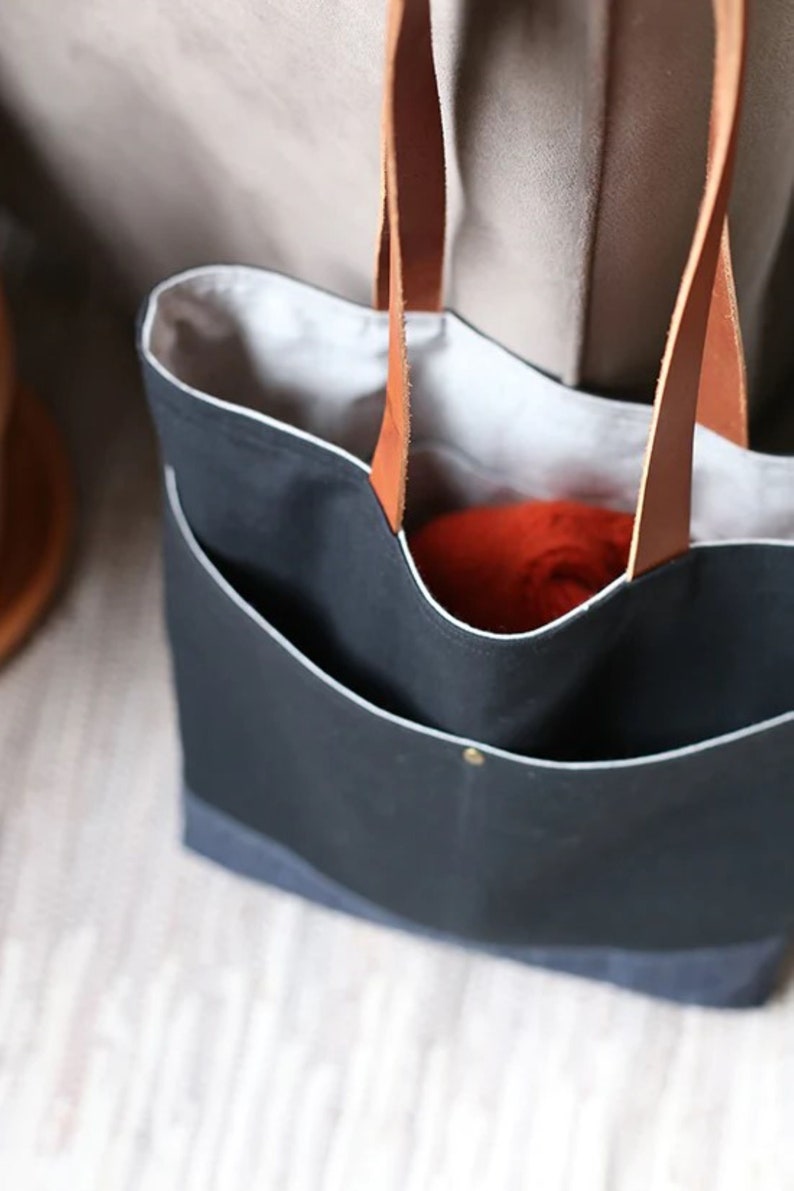 May include: A black canvas tote bag with leather handles. The bag has a white lining and a small pocket on the front. The bag is empty.