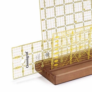 May include: A set of four clear acrylic quilting rulers with yellow markings, including a 15cm ruler, a 30cm ruler, a 30cm square ruler, and a 15cm square ruler. The rulers are displayed on a wooden stand.