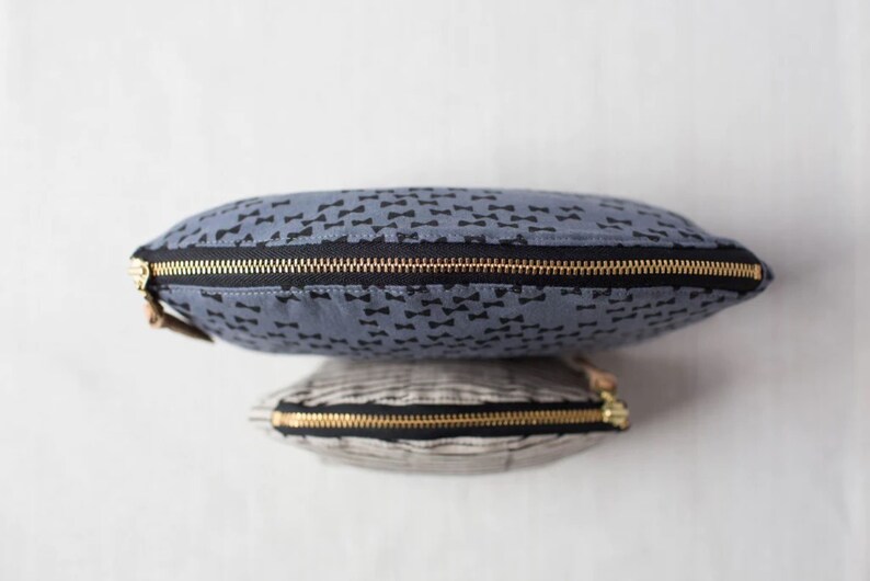 May include: Two zippered pouches, one blue with a black bowtie pattern and one striped in black and white.