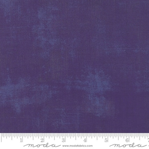 May include: A close-up of a purple fabric with a subtle blue and gray mottled pattern. The fabric is textured and has a slightly distressed look. The fabric is marked with a ruler and the word "moda" appears twice on the ruler.
