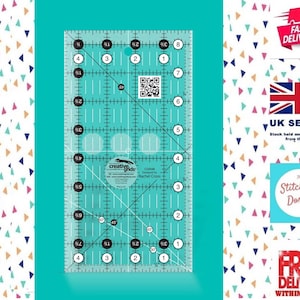 May include: A clear plastic ruler with a turquoise grid and a circle in the centre. The ruler is marked with inches and fractions of an inch. The circle has the text "Creative Grids" and "Designed for Rachel Cross" inside.