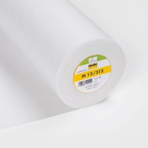 Puede incluir: Un rollo blanco de entretela fusible con una etiqueta amarilla que dice "M 12/312".
