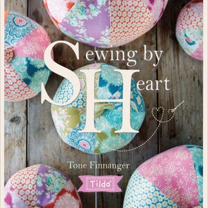 May include: A book cover titled "Sewing by Heart" featuring colorful, patchwork fabric pumpkins. The pumpkins are in shades of pink, purple, orange, and blue, with floral and geometric patterns. The author's name, Tone Finnanger, and the Tilda logo are also visible.