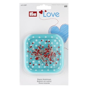May include: A blue and white polka dot magnetic pin cushion with red headed pins. The cushion is in a plastic package with the Prym Love logo.