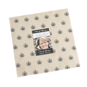 Könnte beinhalten: Ein quadratisches Stoffstück mit cremefarbenem Hintergrund und einem sich wiederholenden Muster aus schwarzen Bienenkorb-Designs. Eine kleine Karte mit dem Text "Bloom & Grow" und dem Bild einer Frau liegt obenauf. Die Marke "Moda Fabrics & Supplies" ist ebenfalls sichtbar.