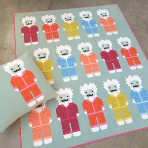 Può includere: Un set di trapunte e cuscini azzurri con un motivo ripetuto di figure pixelate colorate. Le figure sono vestite con vari colori, tra cui rosso, arancione, giallo e blu, con capelli e volti bianchi. La trapunta ha un bordo rosa.