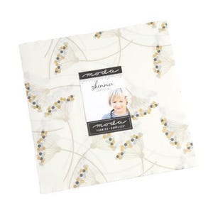 Puede incluir: Una tela blanca con un patrón sutil de puntos grises y dorados sobre tallos delgados. La tela está etiquetada "Moda Shimmer 25" en un rectángulo negro.