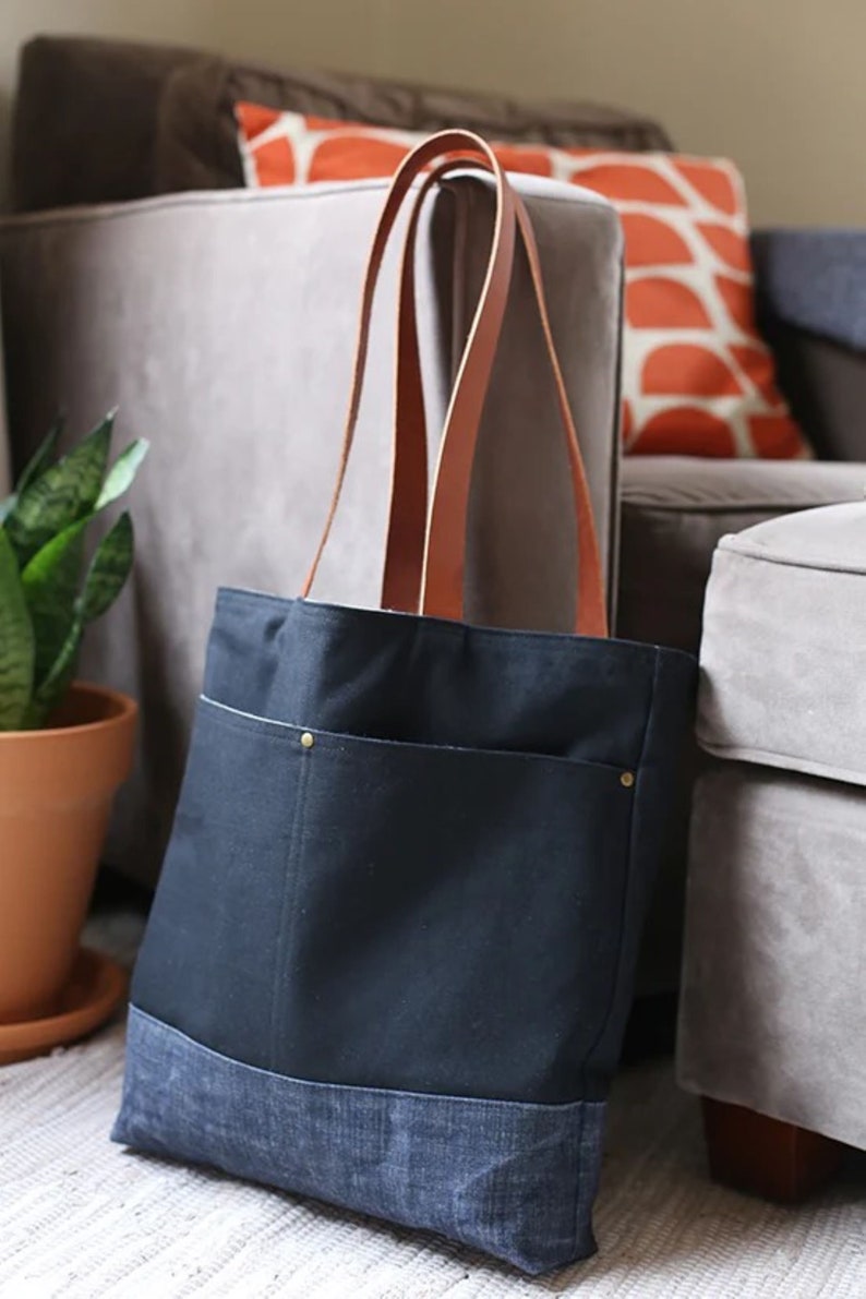 May include: A black canvas tote bag with a denim bottom and brown leather straps. The bag has two front pockets with brass rivets.
