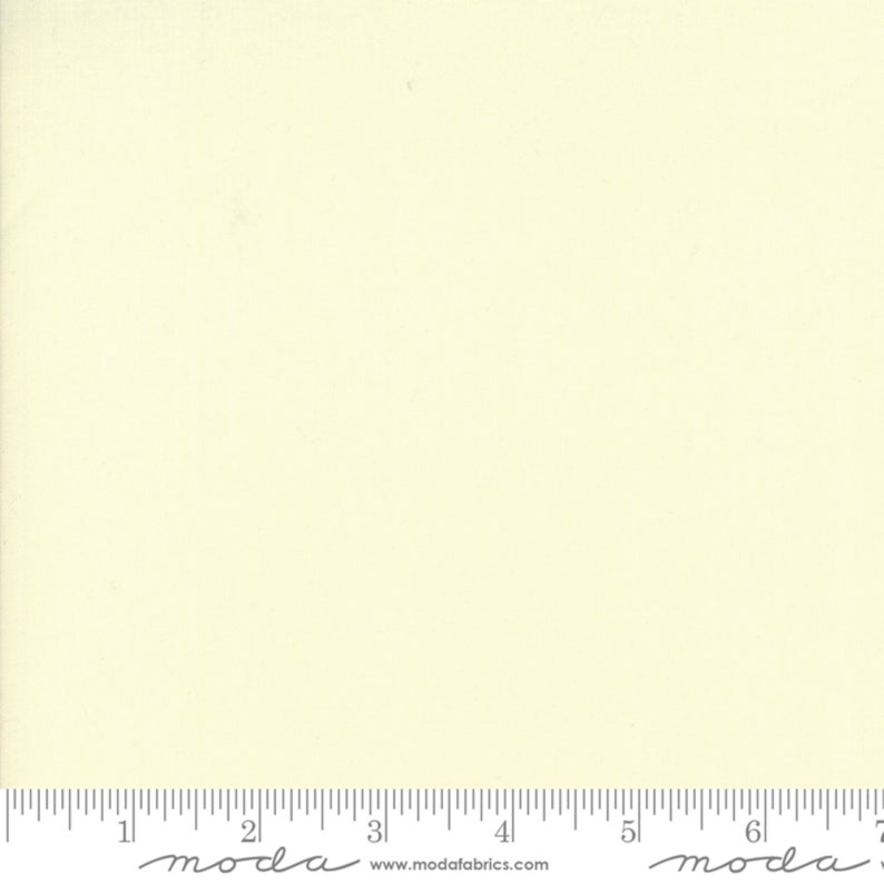 May include: A solid, pale yellow fabric swatch with a ruler underneath. The ruler is marked with inches and has the text "moda" printed on it.