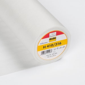 Puede incluir: Un rollo de tela blanca con una etiqueta que dice "Vlieseline H 410/316". La etiqueta es amarilla y roja con texto negro. La tela mide 90 cm x 25 m y está hecha de 70% PA, 30% PES.