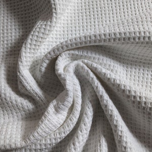 May include: White waffle weave fabric with a textured pattern. The fabric is folded and draped, creating a soft and inviting look.