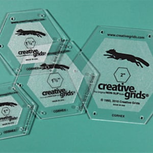 May include: Three clear plastic hexagon-shaped quilting rulers with a fox graphic and the text "creative grids" on each. The rulers are 2.5 cm, 3.8 cm, and 5 cm in size.