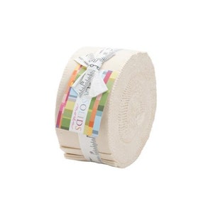 Könnte beinhalten: Eine Rolle Moda Solids Stoff in Creme. Der Stoff ist um einen Pappkarton gewickelt und mit einem Band gebunden. Das Etikett auf dem Stoff lautet "Moda Solids" in einer bunten Schrift.