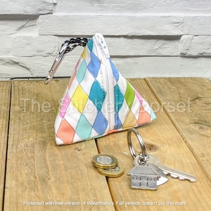 May include: A small, triangular zippered pouch with a colorful diamond pattern in shades of pink, yellow, blue, and green. The pouch has a silver zipper and a silver clip attached to a black cord.