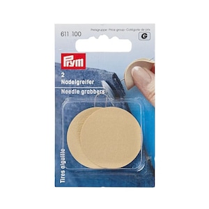 Pode incluir: Um pacote de dois pegadores de agulha bege. A embalagem tem o texto "PRYM" e "Needle grabbers". Os pegadores de agulha são redondos e feitos de um material texturizado. A embalagem também inclui o texto "Tires aiguille".