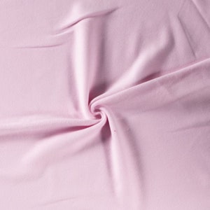 Puede incluir: Primer plano de una tela suave y rosa con una textura lisa. La tela está doblada y drapeada, creando un efecto suave y fluido.