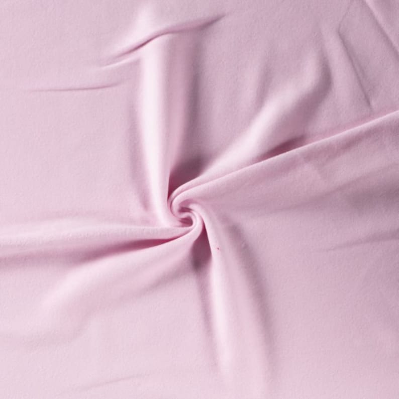 Puede incluir: Primer plano de una tela suave y rosa con una textura lisa. La tela est&aacute; doblada y drapeada, creando un efecto suave y fluido.