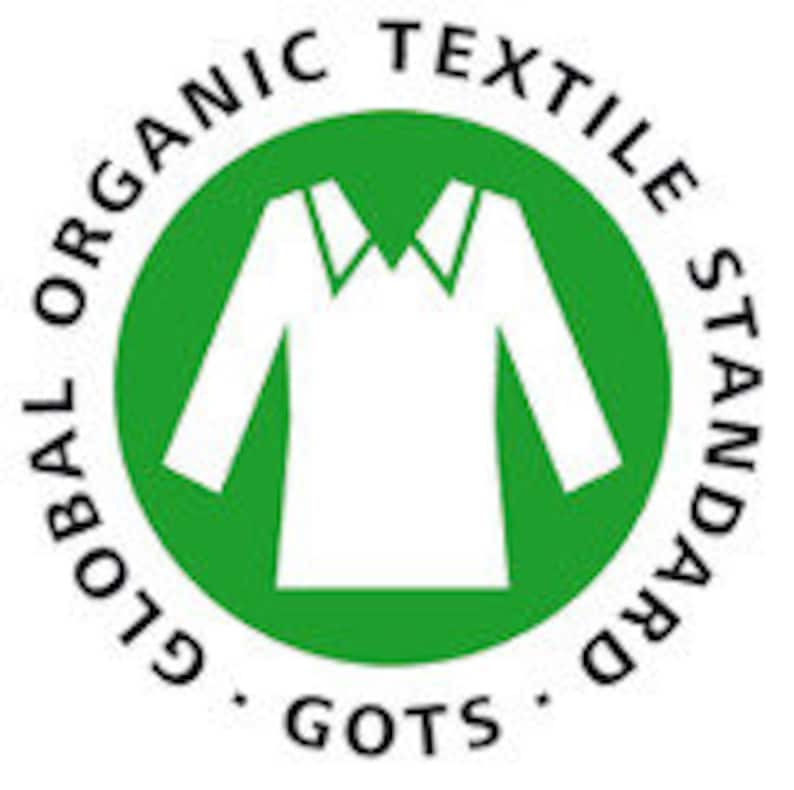 Puede incluir: Un c&iacute;rculo verde con el texto "GLOBAL ORGANIC TEXTILE STANDARD" que rodea una silueta blanca de una camisa de manga larga. El texto "GOTS" est&aacute; en la parte inferior del c&iacute;rculo.