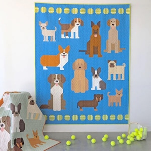 Op de afbeelding: Een blauwe quilt met een patroon van verschillende hondenrassen. De honden zijn allemaal in een geometrische stijl en worden omringd door een rand van groene tennisballen.