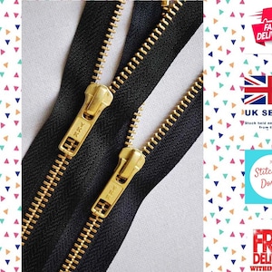 May include: Two black zipper tapes with gold metal teeth and sliders. The zippers are laid out side by side, with the sliders facing each other. The zippers are labelled "YKK" on the sliders.