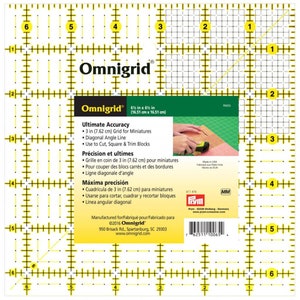 May include: A yellow and white 6-inch by 6-inch Omnigrid ruler with a grid pattern. The ruler has markings in inches and centimetres. The ruler is designed for cutting, squaring, and trimming fabric.