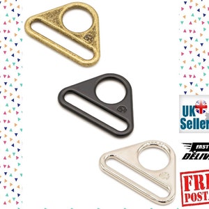 Op de afbeelding: Drie metalen D-ringen in goud, zwart en zilver. Elke ring heeft een driehoekige vorm met een cirkelvormige opening en een rechthoekige staaf. De ringen worden weergegeven op een witte achtergrond met een kleurrijk driehoekpatroon.
