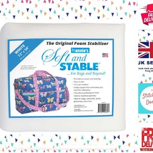 Op de afbeelding: Een witte verpakking van ByAnnie's Soft and Stable schuimstabilisator van 183 cm bij 147 cm. De verpakking bevat tekst, een streepjescode en een afbeelding van een blauwe reistas met een kleurrijk vlinderpatroon en roze riemen.