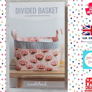 May include: A sewing pattern for a divided basket with a pink and white floral fabric. The pattern is titled "Divided Basket" and is by Noodlehead.