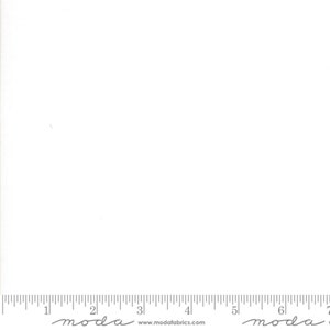 May include: A plain white fabric swatch with a ruler at the bottom. The ruler is marked in inches and has the text "moda" printed on it.