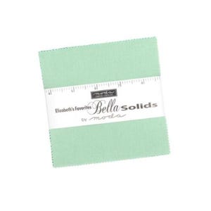 Puede incluir: Un conjunto de cuadrados de tela verde claro, sujetos con una banda de papel blanca. La banda muestra el texto "Elizabeth's Favorites Bella Solids by moda" y un gráfico de regla. La tela parece ser de algodón, adecuada para acolchar.