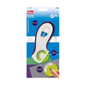 May include: A white and purple ergonomic rotary cutter with a 45mm blade. The cutter has a soft handle and a blade protection mechanism. The packaging includes the Prym logo and the text "Rollschneider Rotary cutter".